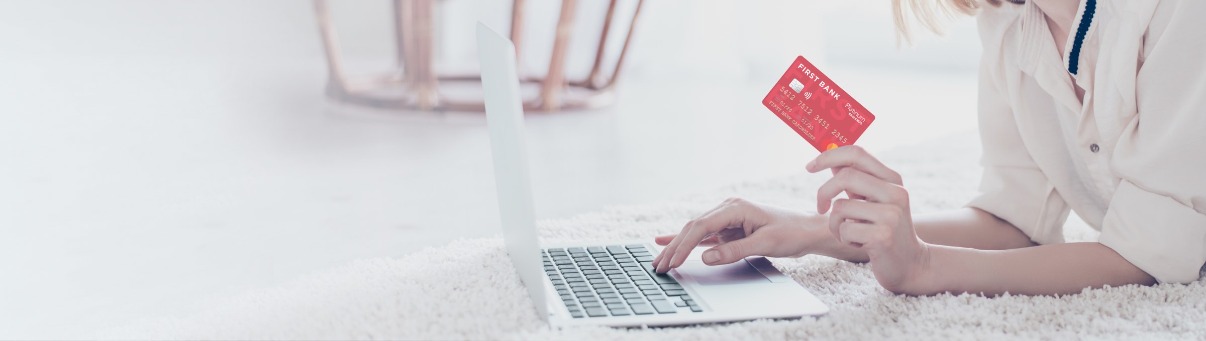 a woman holding her Easthigh Credit Union Platinum Rewards card while on the computer.